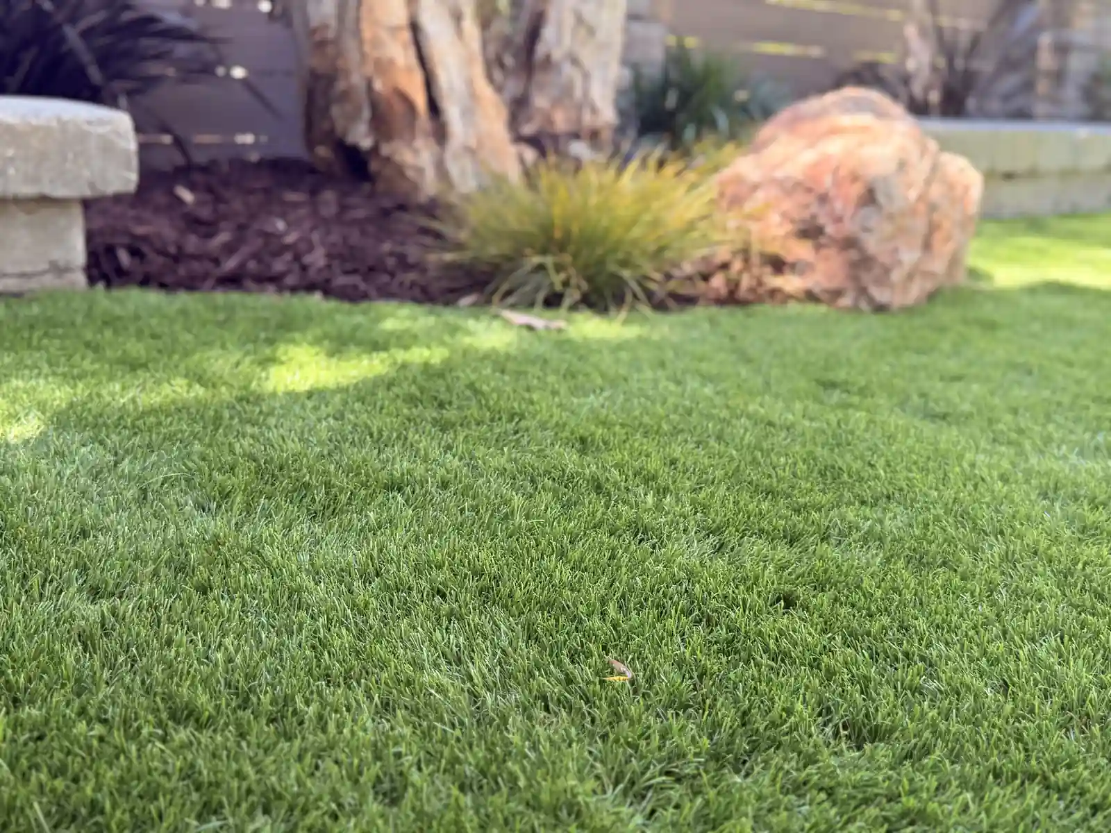 Close-up of lush artificial turf with boulder accents by Panjia Outdoors